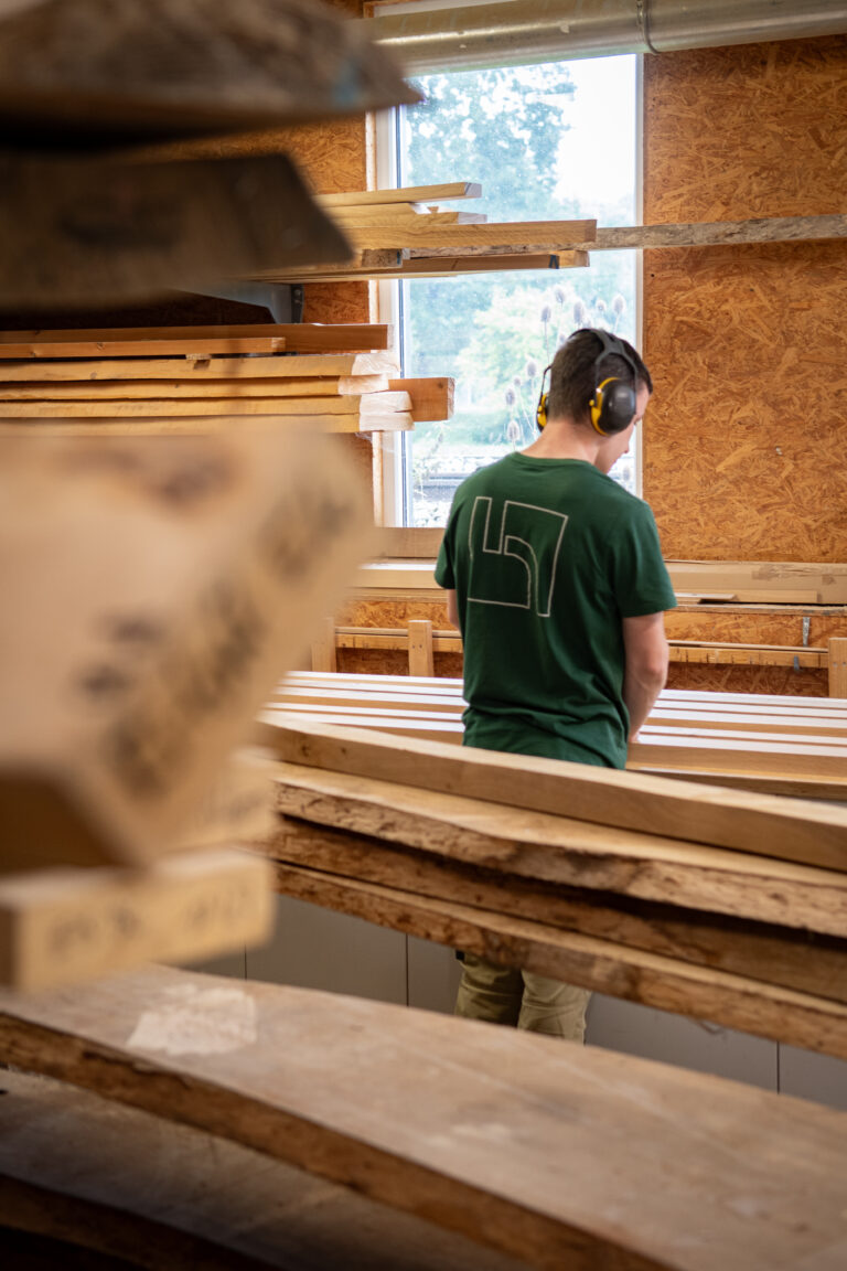 Präzise Holzverarbeitung: Schreinerei-Huber-Mitarbeiter begutachtet nach Maß gefertigte Massivholzbohlen in der Werkstatt.
