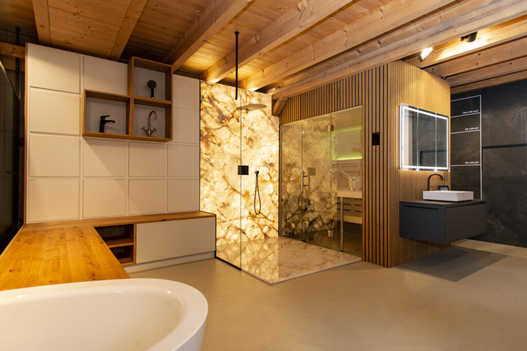 Ein Blick in den Badezimmer- und Saunabereich unserer Austsellung. Neben der Sauna ist die offene Dusche mit beleuchteter Natursteinplatte als Rückwand ein klares Highlight.
